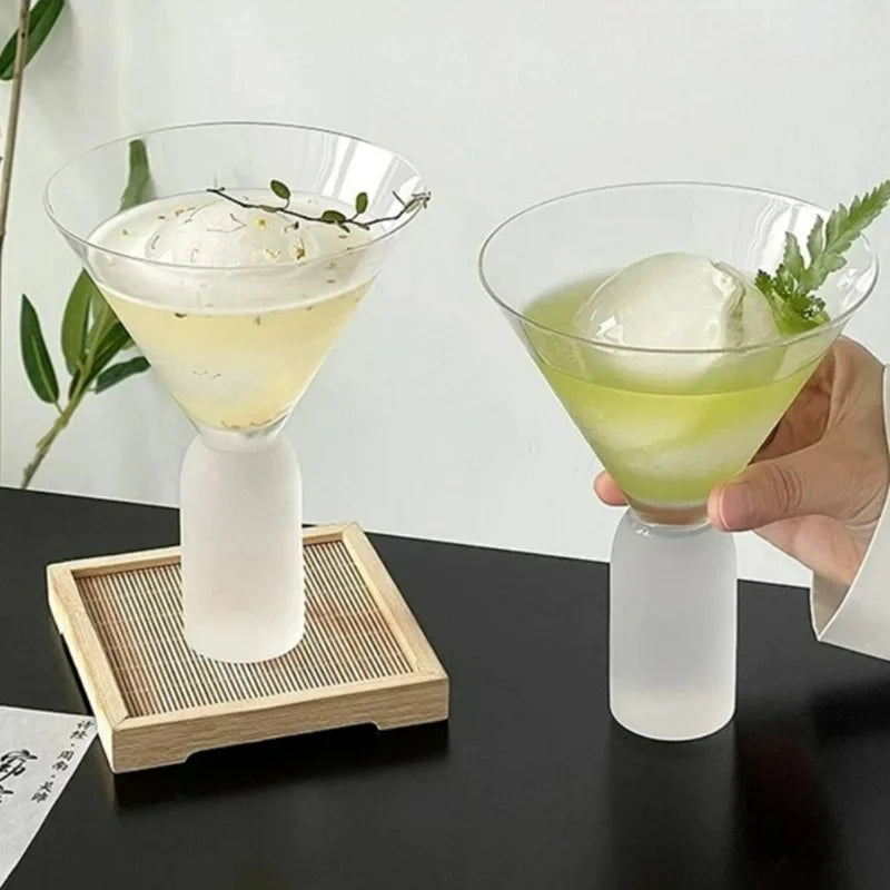 empty frosted base martini glass held in hand over black tabletop