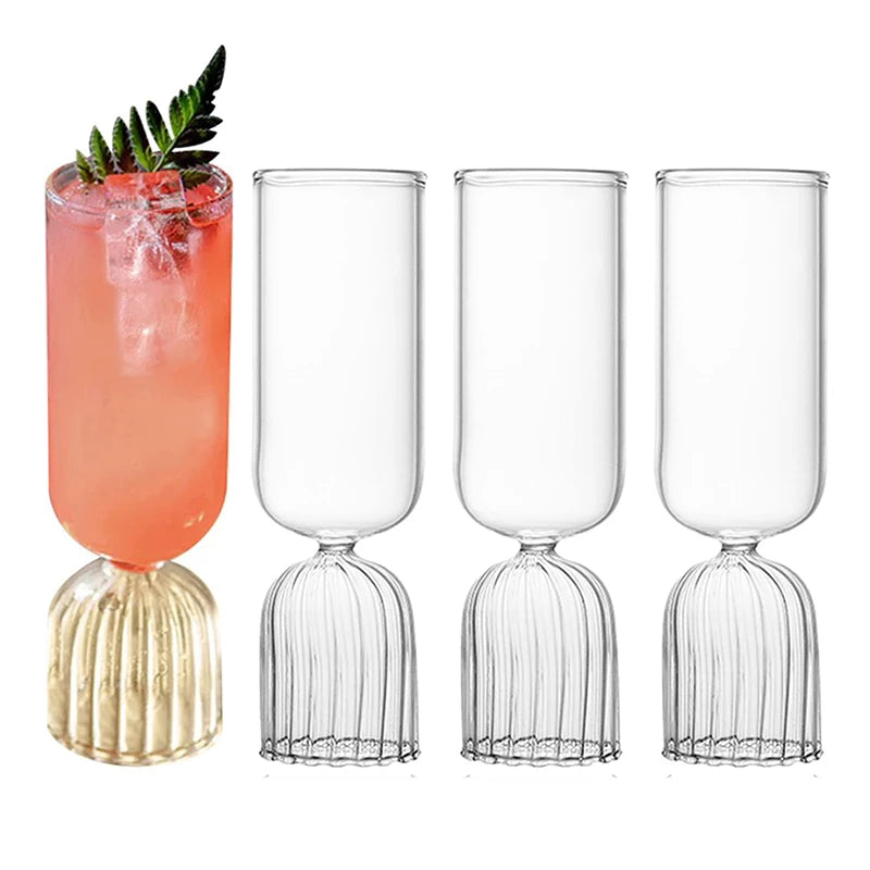 Tall modern cocktail glass with ribbed pedestal base filled with pink drink and ice
