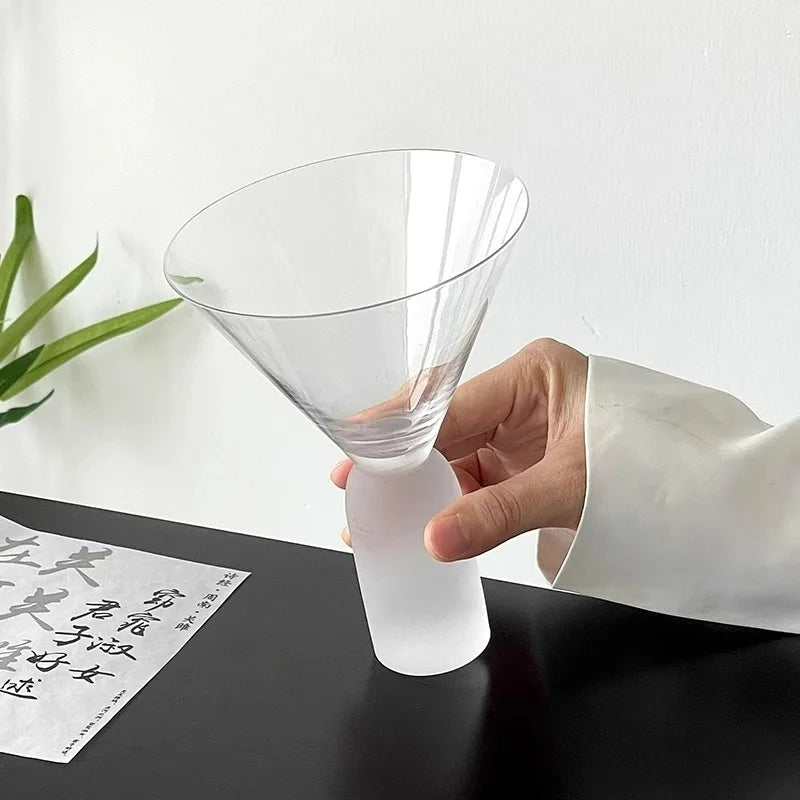 clear martini glass on ribbed frosted base holding orange cocktail with garnish