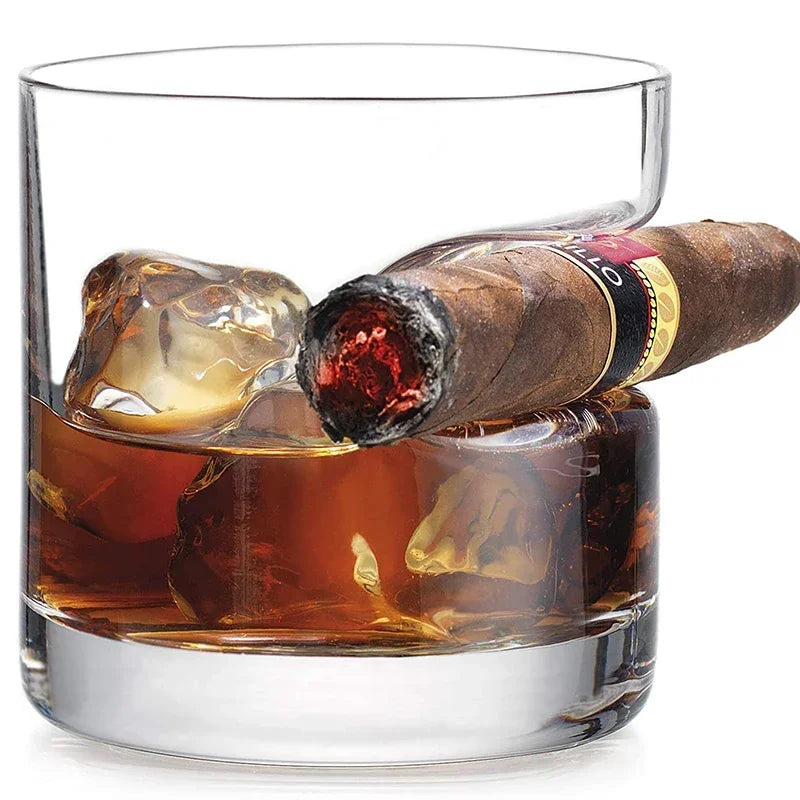 Old fashioned whiskey glass with indented cigar rest holding lit cigar on ice