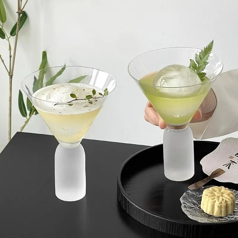 tall frosted stem martini glass with pink cocktail and ice on brass table