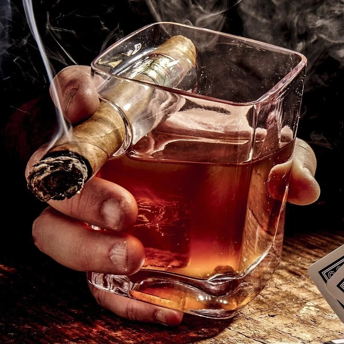 Hand holding whiskey and cigar glass during poker night